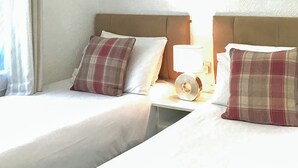 Twee enkele bedden met hoofdborden, een bedlampje en een raam met gordijnen.