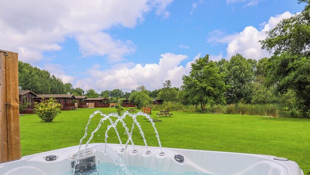 Een jacuzzi met waterstralen, omgeven door een gazon en bomen, met een houten hek en een picknicktafel op de achtergrond.
