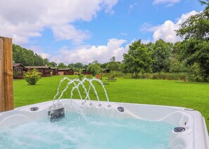 Een jacuzzi met waterstralen, omgeven door een gazon en bomen, met een houten hek en een picknicktafel op de achtergrond.