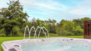 Een jacuzzi met meerdere waterstralen, omgeven door een weelderige groene tuin en bomen.