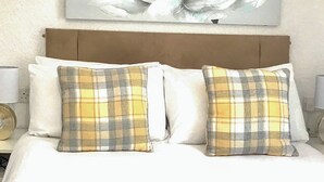 Een bed met twee geruite kussens, een houten hoofdbord en een kunstwerk aan de muur.