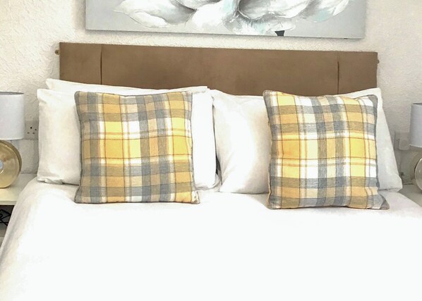 Een bed met twee geruite kussens, een houten hoofdbord en een kunstwerk aan de muur.