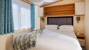 A bedroom with a bed, a nightstand, a lamp, a window with curtains, and a radiator.