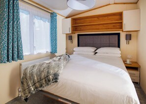 A bedroom with a bed, a nightstand, a lamp, a window with curtains, and a radiator.