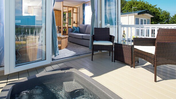 A deck with a hot tub, wicker furniture, and a glass door leading to an interior space with a sofa and a dining area.