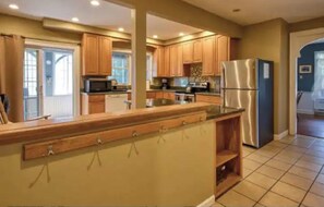 A spacious kitchen with wooden cabinets, a stainless steel refrigerator, and a large island with hooks.