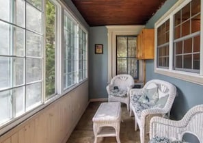 A covered porch with wicker furniture, large windows, and a wooden ceiling.