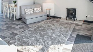 A living room with a grey sofa, patterned rug, white radiator, and a black heater. - 2 Bedroom Apartment with Hot Tub (Thirsk)