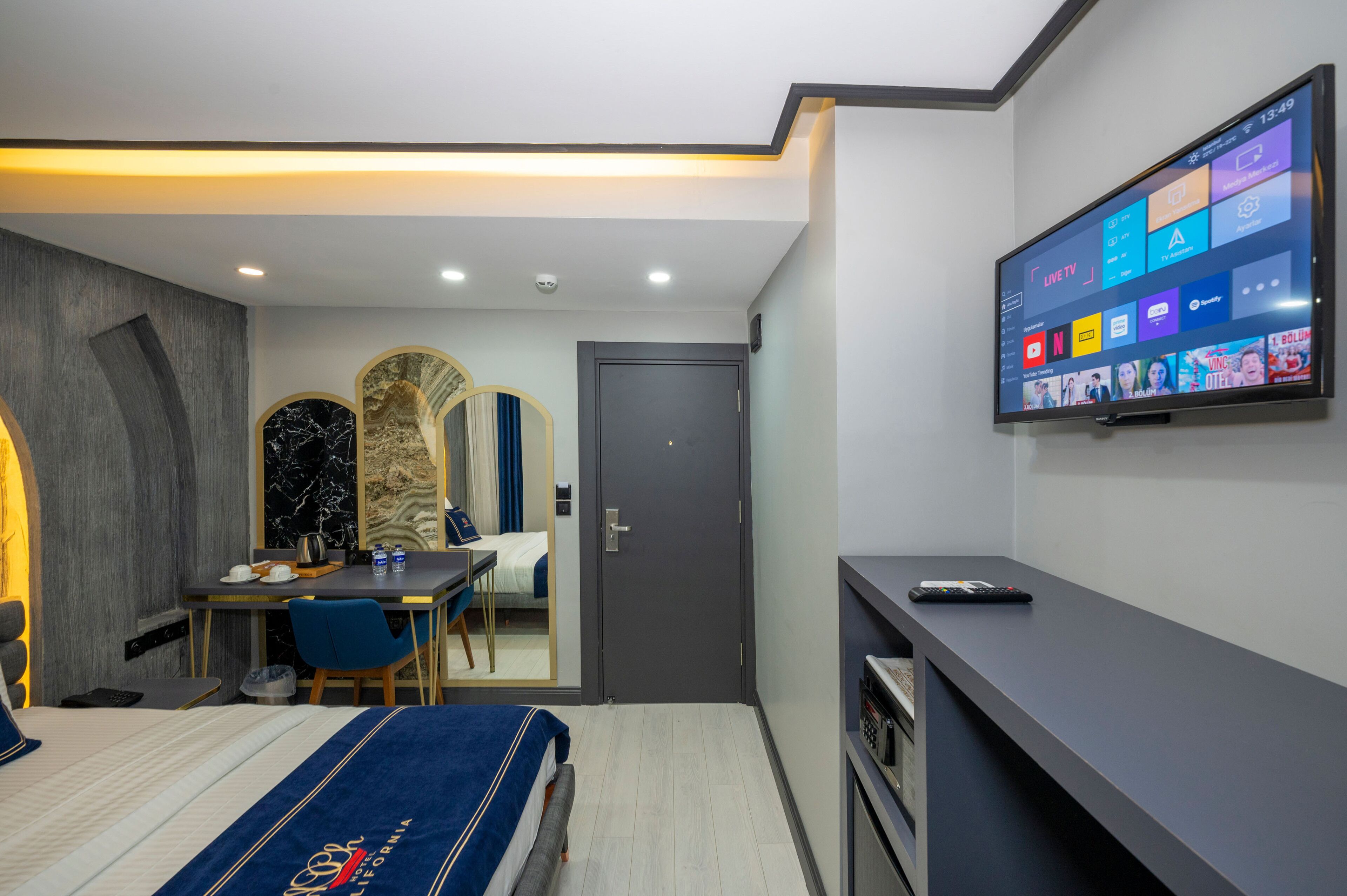 Ein modernes Hotelzimmer mit Bett, Schreibtisch und Fernseher, der verschiedene Sender anzeigt.