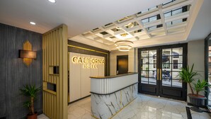 A hotel reception area with a marble counter, a modern ceiling design, and a view of the outside through large windows. - California Hotel (Istanbul)