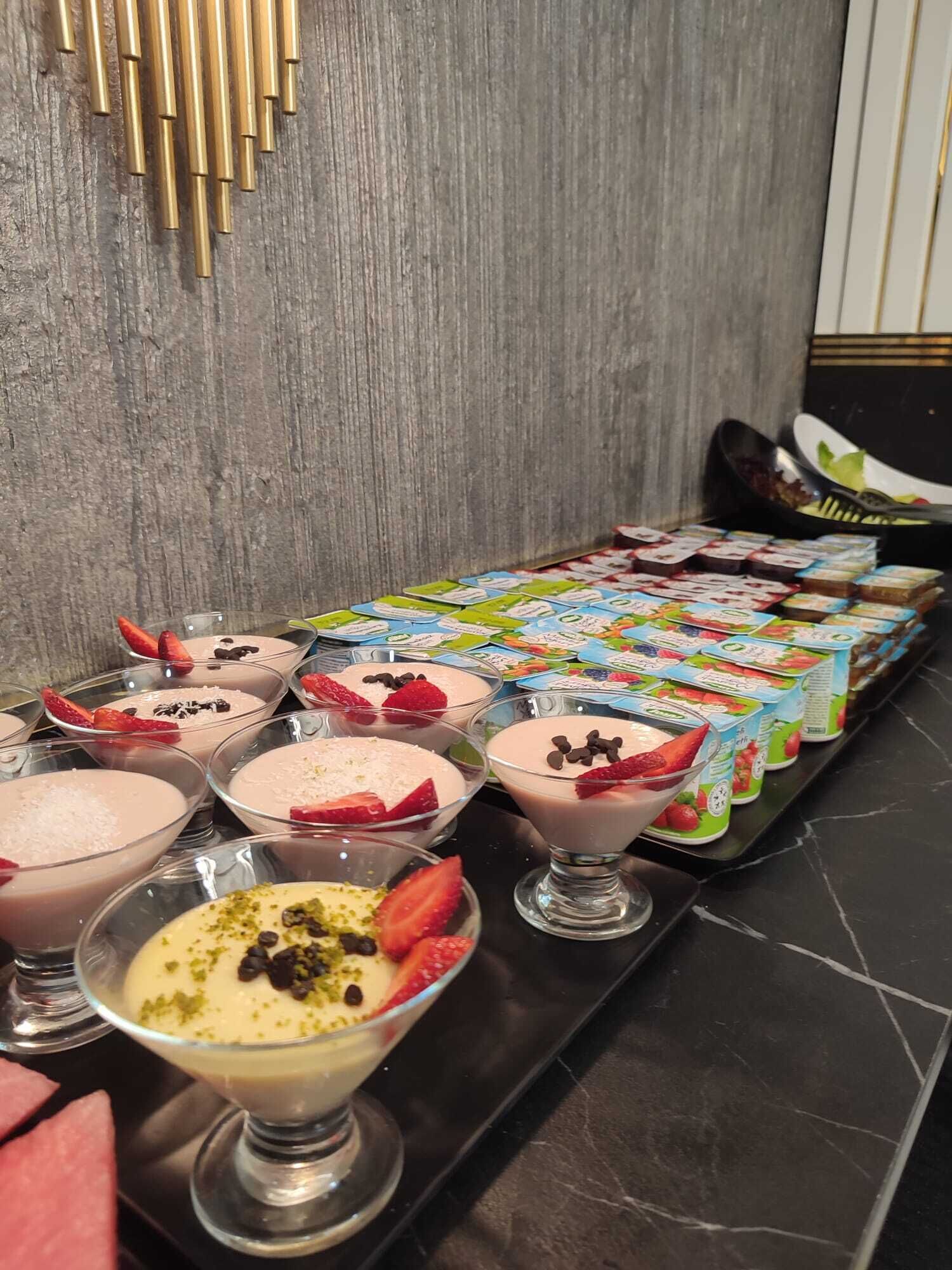 Un bufé de postres con diversos dulces cubiertos de fruta y yogures envasados.