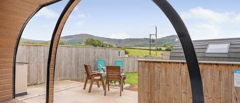 Un patio con una mesa y sillas de madera, un jacuzzi y vistas al campo.