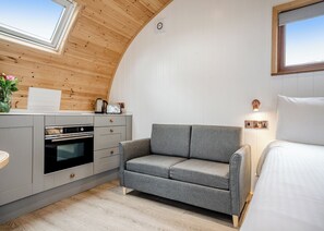Quarto aconchegante com cozinha compacta, sofá cinza, cama e um claraboia.