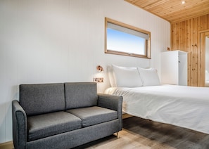 Quarto com sofá cinzento, cama com roupa de cama branca, guarda-roupa de madeira e espelho fixado na parede.