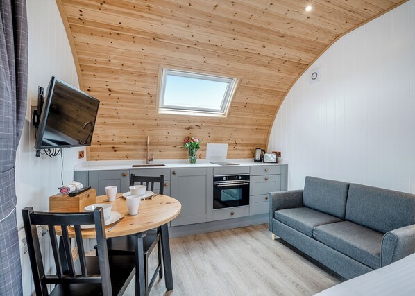 A compact kitchen with a wooden ceiling, a dining table with chairs, a grey sofa, and a small window. - 0 bedroom accommodation in Great Busby (Great Busby)