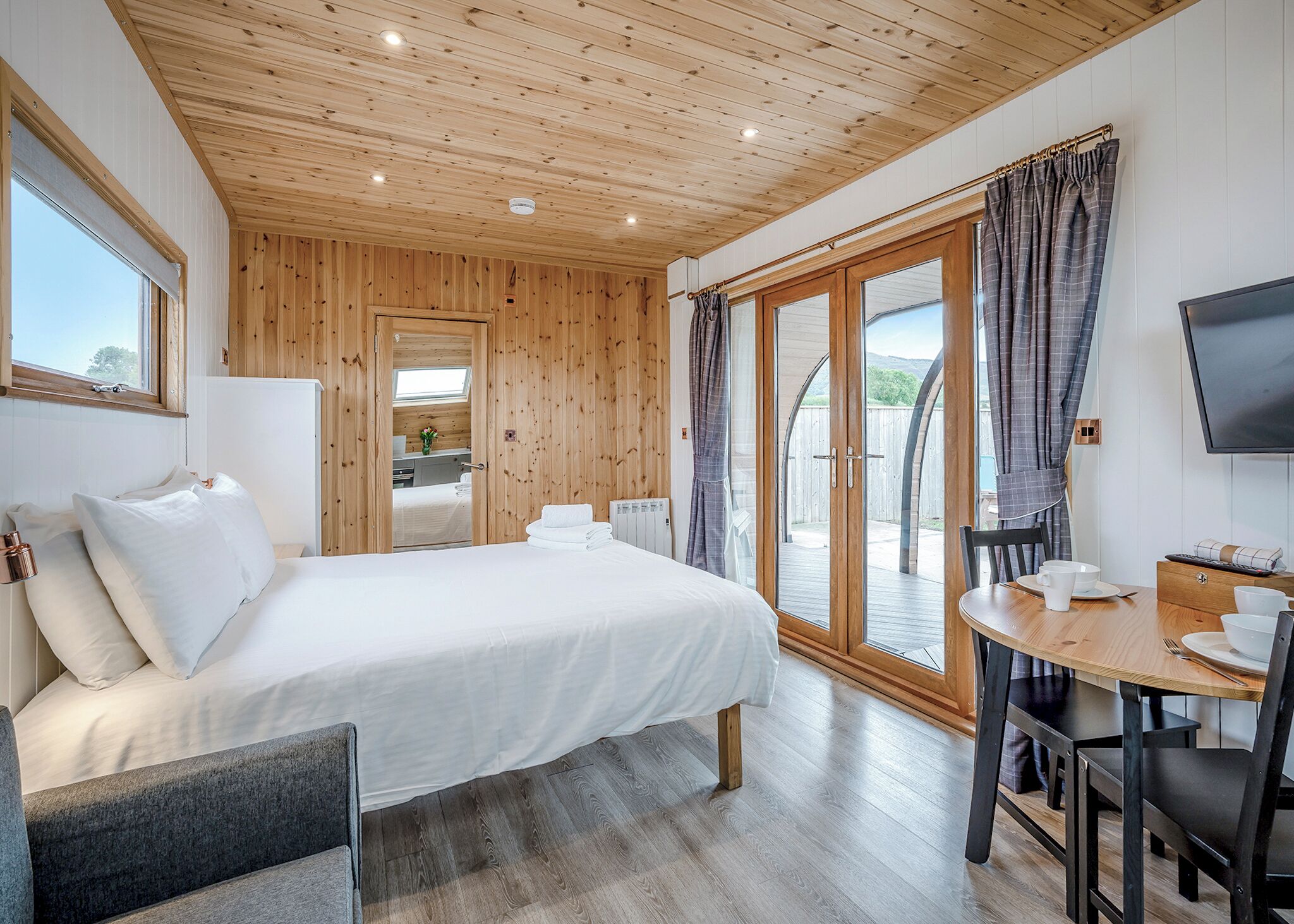 A bedroom with a bed, a desk, a chair, a TV, and a sliding glass door to an outdoor area.