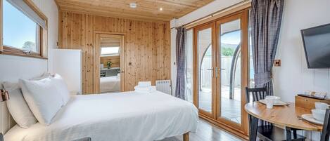 A bedroom with a bed, a desk, a chair, a TV, and a sliding glass door to an outdoor area.