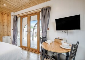 A room with a bed, a dining table with chairs, a TV mounted on the wall, and a sliding glass door leading to an outdoor area. - 0 bedroom accommodation in Great Busby (Great Busby)