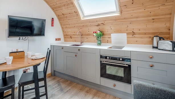 Une cuisine moderne avec un plafond en bois, un four encastré, un évier et un coin repas comprenant une table et des chaises.
