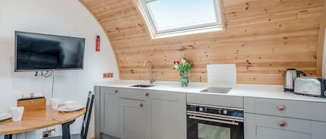 A modern kitchen with a wooden ceiling, a built-in oven, a sink, and a dining area with a table and chairs.