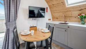 Een compacte keuken met een houten plafond, een flatscreen televisie boven de aanrecht en een eettafel met stoelen.