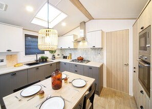 A modern kitchen with grey cabinets, a wooden dining table set for four, and a large window above the sink.
