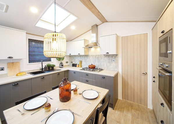A modern kitchen with grey cabinets, a wooden dining table set for four, and a large window above the sink.
