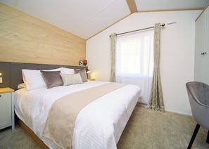 A bedroom with a bed, bedside tables, a chair, a window with curtains, and a headboard.