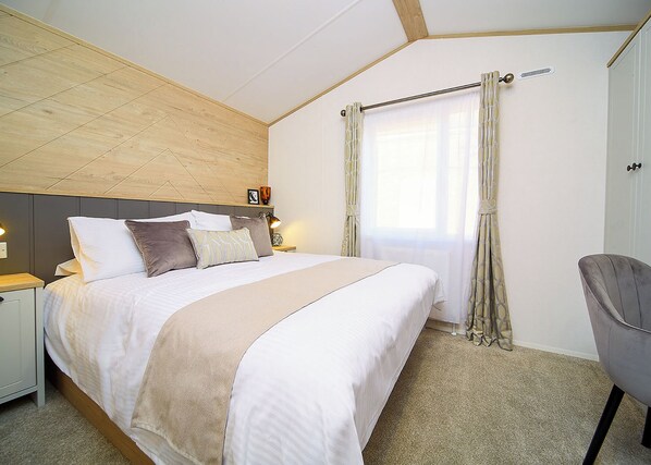 A bedroom with a bed, bedside tables, a chair, a window with curtains, and a headboard.