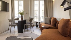Ein modernes Wohnzimmer mit einer Couch, Sesseln, einem Esstisch und einem an der Wand befestigten Fernseher.