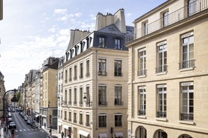 En gatubild som visar en parisisk byggnad med flera våningar, stora fönster och balkonger.
