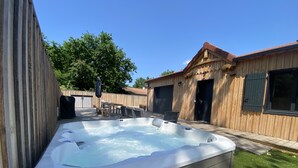 A hot tub in a backyard with a wooden fence, a covered table, and a garage. - Wooden villa with pool (Arès)