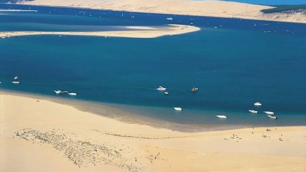 A coastal landscape with a sandy beach, calm blue waters, and boats. - Wooden villa with pool (Arès)