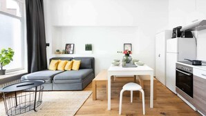 Ein modernes Wohnzimmer mit grauem Sofa, einem kleinen Esstisch und einer Küchenzeile mit Herd und Backofen.