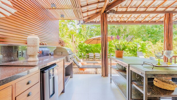 A modern outdoor kitchen with a built-in grill, dining area with chairs and a table, and a view of lush greenery. -  PF41 House 6 Bedrooms 300m from the Sea (Mata de São João)