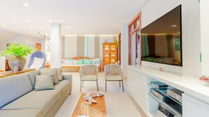 A modern living room with a sofa, chairs, a TV, and a cabinet with electronic devices. -  PF41 House 6 Bedrooms 300m from the Sea (Mata de São João)
