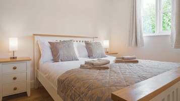 A neatly made bed with a patterned bedspread, two bedside lamps, a wooden nightstand, and a window with curtains.