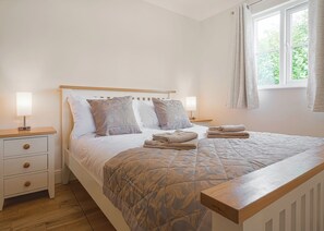 A neatly made bed with a patterned bedspread, two bedside lamps, a wooden nightstand, and a window with curtains. - 2 bedroom accommodation in Palgrave, Diss (Palgrave, Diss)
