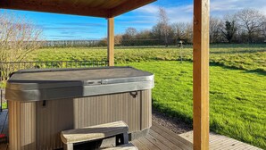 Una vasca idromassaggio sotto un gazebo in legno, con un prato e alberi sullo sfondo.