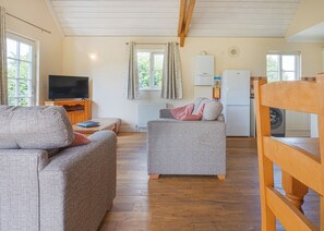 A cozy living room with a sofa, a small table, a television, and a kitchen area with a refrigerator and a washing machine. - 2 bedroom accommodation in Palgrave, Diss (Palgrave, Diss)