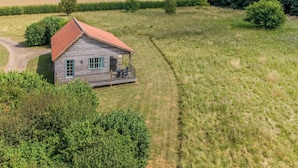 A wooden cabin with a red roof, surrounded by a grassy field and trees. - 1 bedroom accommodation in Palgrave, Diss (Palgrave, Diss)