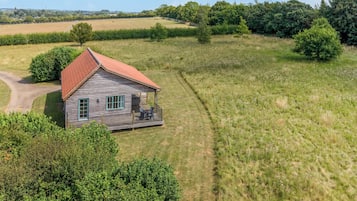 A wooden cabin with a red roof, surrounded by a grassy field and trees.