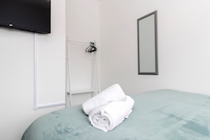 Habitación de hotel con cama, televisión montada en la pared, toalla, espejo y perchero.