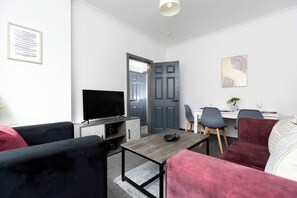 Un salon moderne doté d’un téléviseur à écran plat, d’un coin repas avec une table et des chaises, et d’une porte grise.