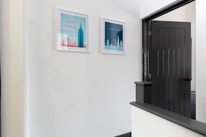 Un pasillo con dos carteles enmarcados de paisajes urbanos, uno que dice 'NEW YORK' y otro 'LONDON', y una puerta negra.