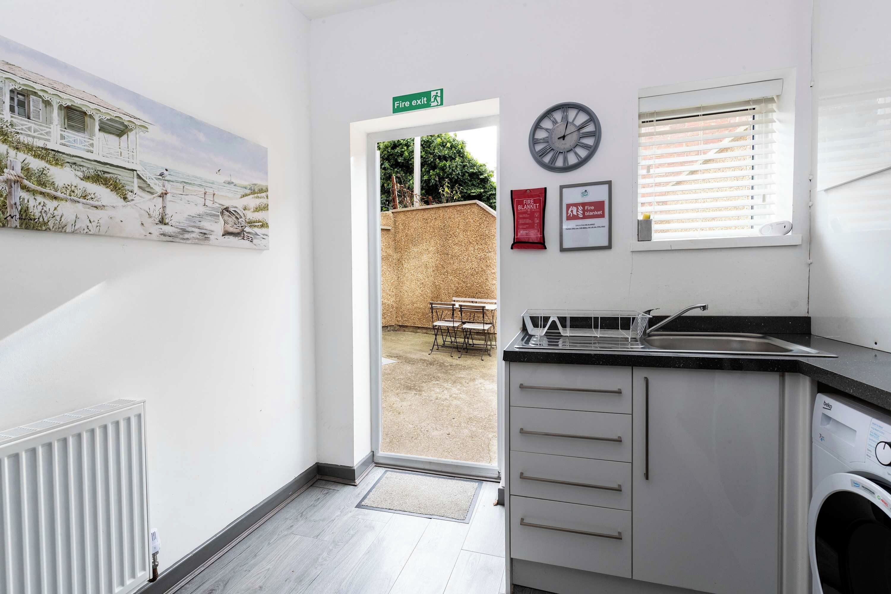A modern kitchen with a washing machine, a clock, and a fire exit sign.