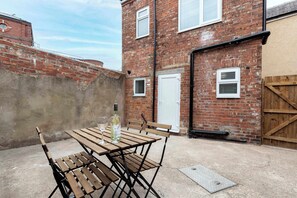 A brick building with a wooden table and chairs, a bottle of wine, and a wooden gate.