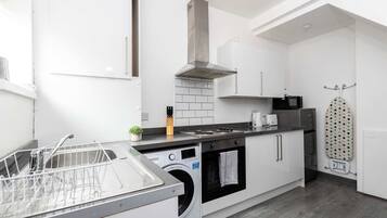 A modern kitchen with a dishwasher, oven, microwave, and a drying rack.