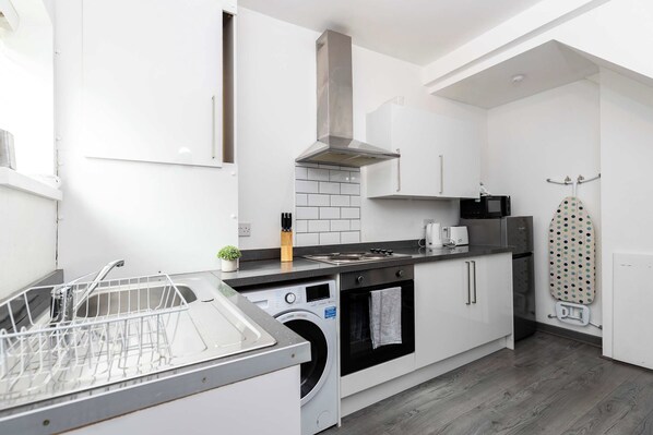 A modern kitchen with a dishwasher, oven, microwave, and a drying rack.