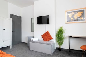Una habitación de hotel moderna con un sofá gris, un televisor de pantalla plana montado en la pared, una mesita con una planta y un mapa del mundo enmarcado en la pared.